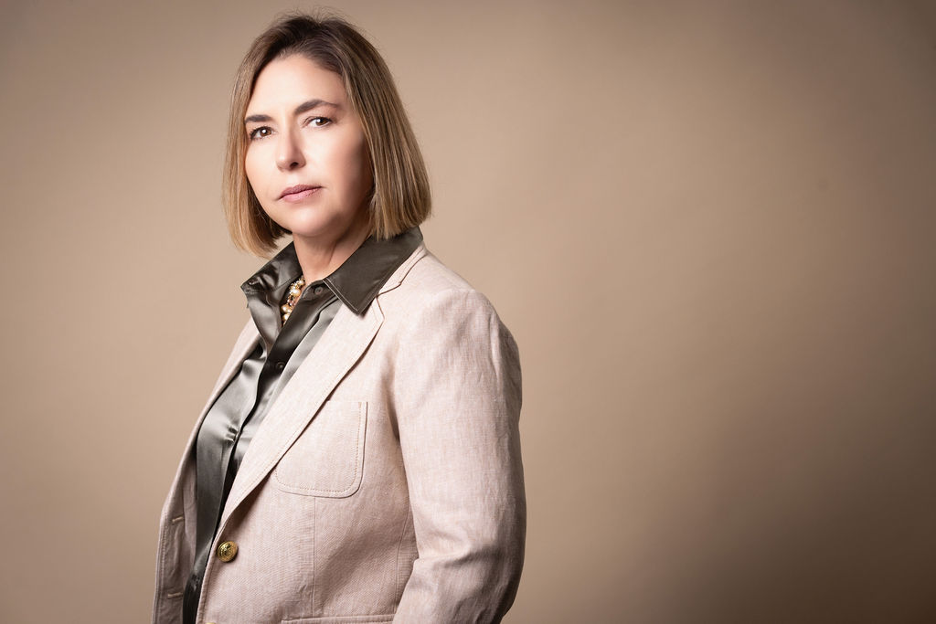 Ingrid Rainey, Managing Partner of Rainey Law P.C., in a cream linen blazer against a warm tan backdrop