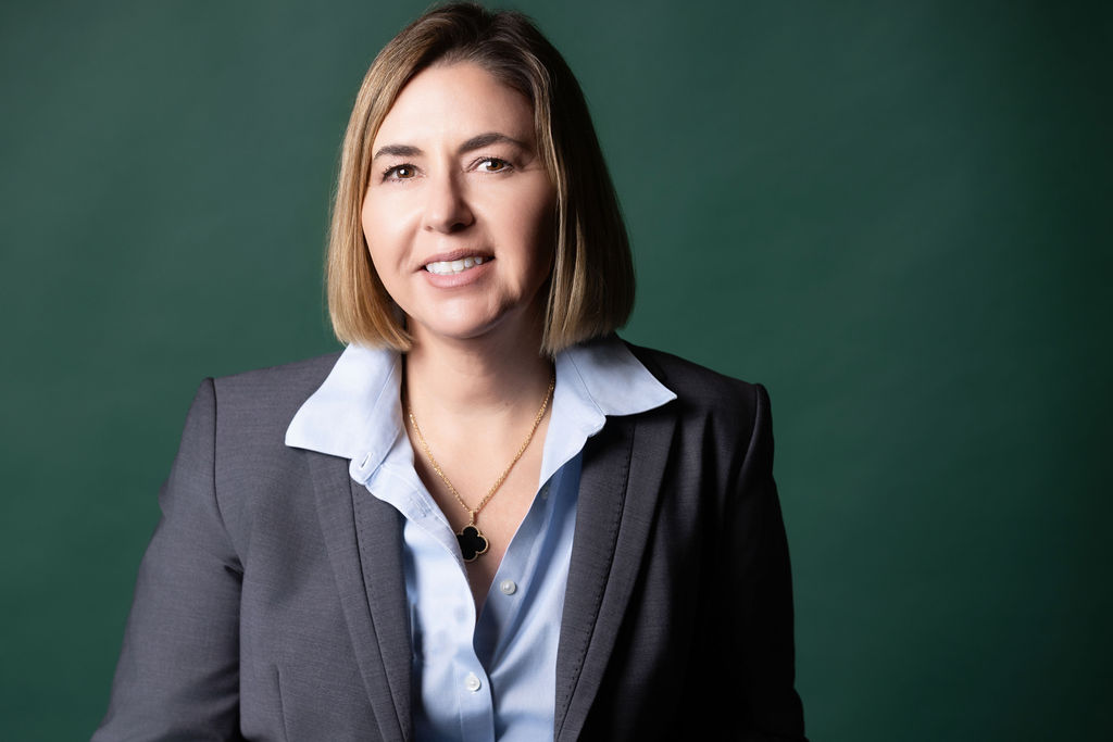 Ingrid Rainey, Managing Partner of Rainey Law P.C., smiling in a tailored suit against a deep green backdrop